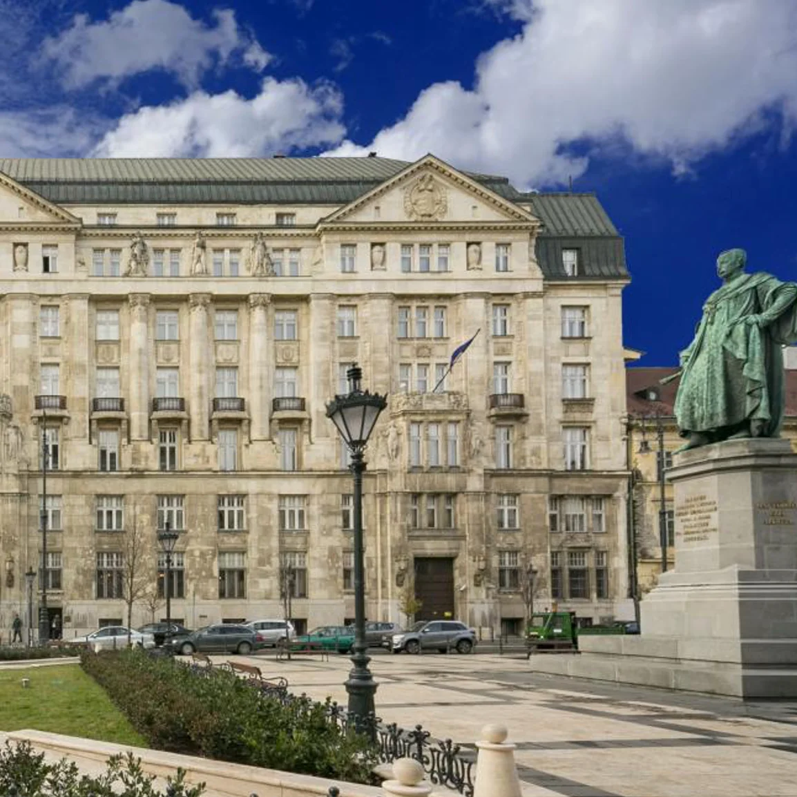 A stone building beside a public square and statue in Budapest